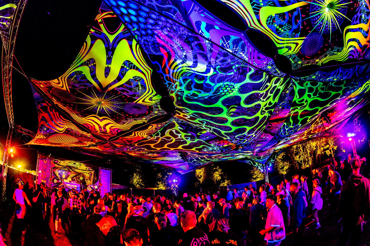 Tanzende Menge unter einer leuchtenden Decke aus psychedelischen Stoffbahnen auf der XPedition Stage.
