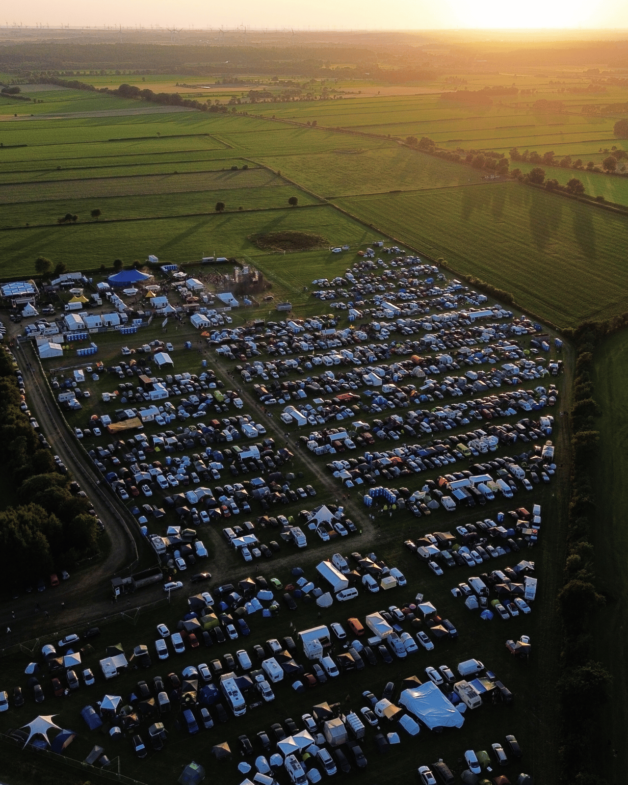 Luftaufnahme des Campingplatzes mit vielen Zelten und Wohnmobilen bei Sonnenuntergang.