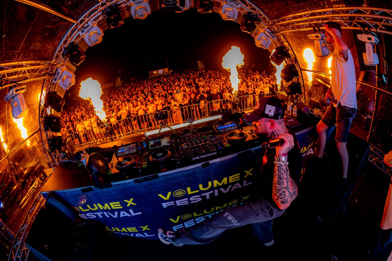 Zwei DJs jubeln auf einer Bühne vor einer großen Menschenmenge und einer Lichtshow.